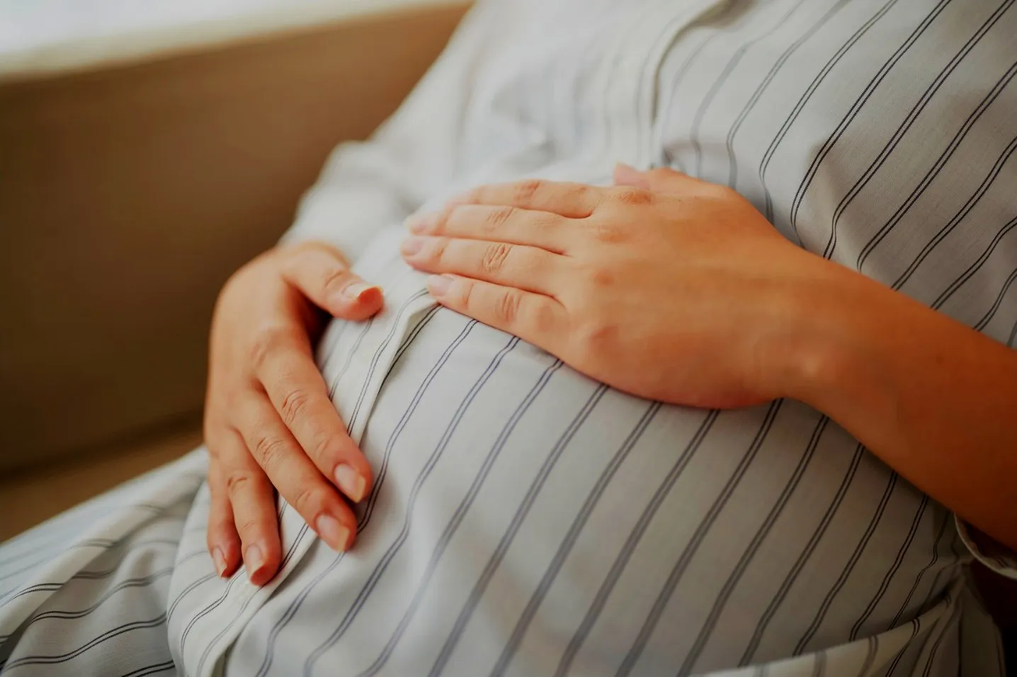 Expecting mother resting her hands on her belly at home