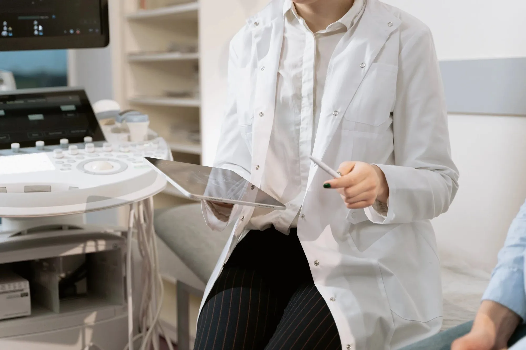 Sonographer in a white coat reviewing results on a tablet beside an ultrasound system